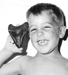 grinning boy holding a large shark tooth